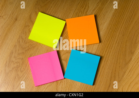 Several blank neon colored post-it notes lying on a wooden floor or desk Stock Photo