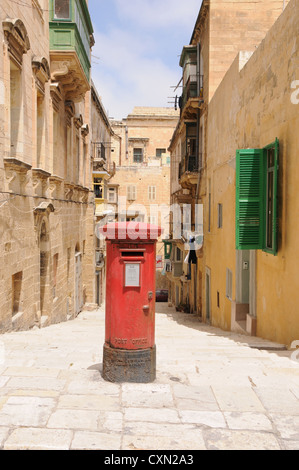 Rusty & faded British red letter box in street in Valetta , Malta. Positioned centrally on residential street in sunlight. Stock Photo