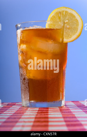 Ice cold glass of iced tea on a gingham checked tablecloth in front of a blue sky background Stock Photo