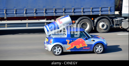 Customised advertising Red Bull brand energy drink by incorporating large can & logo into mini car body driving on M25 motorway road Essex England UK Stock Photo