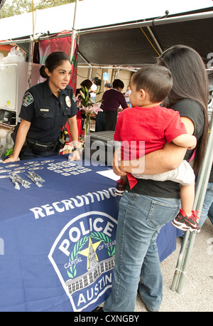 Hispanic female police officer speaks to woman carrying young son at Austin Police Department recruitment booth outdoor festival Stock Photo