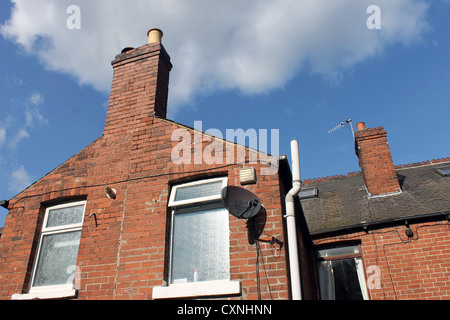 Old brick house or home with chimney and satellite dish, blue sky and cloudscape background. Stock Photo