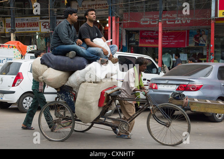 Two young affluent men sitting on top of sacks on an overloaded cycle rickshaw, Chandni Chowk, Old Delhi, India Stock Photo
