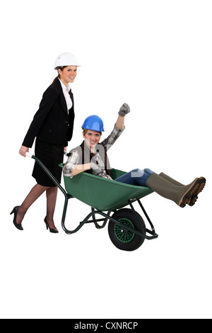 Woman pushing fellow worker in wheelbarrow Stock Photo