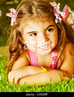 Photo of cute little girl lying down fresh green grass, adorable baby having fun in daycare, pretty cheerful child female