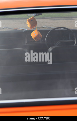 Pair large orange fuzzy furry dice hanging from rear view mirror, restored orange Ford Cortina Mark 3, Suffolk, UK Stock Photo
