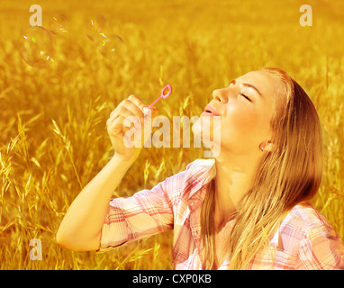 Image of cute blond girl blowing soap bubbles on wheat field, happy teenager having fun on golden crop meadow, closeup portrait Stock Photo