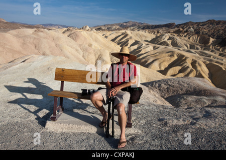 Adult male sits on park bench in front badlands Zabriskie Point Death Valley National Park California United States America Stock Photo
