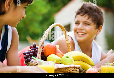 Photo of two happy boy on picnic in park, brothers lying down on meadow and enjoying fresh sweet fruits, teens have lunch Stock Photo
