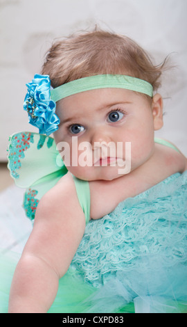 6 month old baby girl wearing turquoise ruffled bloomers and fairy wings strikes a pensive pose. Stock Photo