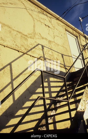 Detail of metal fire escape stairs casting shadows on pale wall in evening light Stock Photo