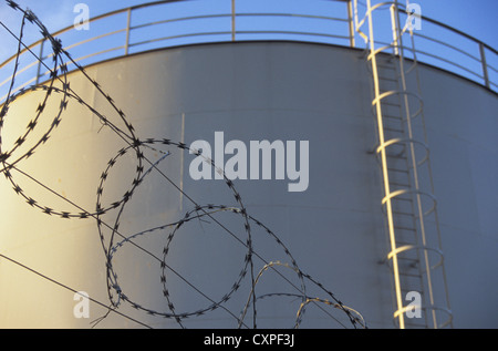 Detail of large oil or chemical storage tank with its ladder and security fence of wire and razor wire in front Stock Photo