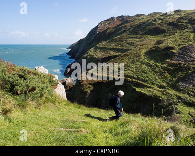 Person walking down steep stepped section of Isle of Anglesey Coastal Path with view of rugged coastline at Hell's Mouth. Cemaes Anglesey Wales UK Stock Photo