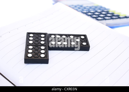 Black plastic dominoes on notebook with calculator. Stock Photo
