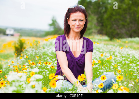 Mid adult woman sitting in a field of flowers Stock Photo