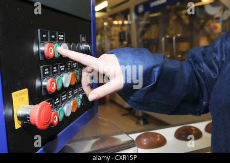 Woman's finger pushing a green button for go by a conveyor belt with chocolate eggs on it in a chocolate factory Stock Photo