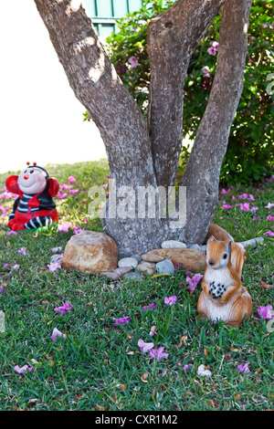 Two small decorative figures in the shape of a ladybug and squirrel, used as garden gnomes in the lawn under a tree Stock Photo