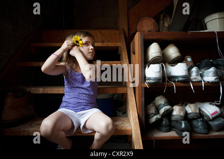 Little girl on basement steps, putting a flower in her hair Stock Photo