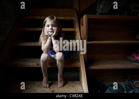 Little girl sitting on basement steps, looking at camera