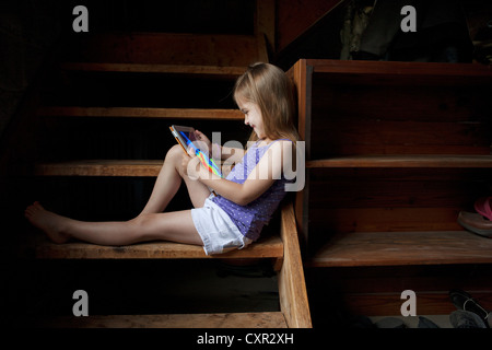 Little girl sitting on basement steps, looking at digital tablet