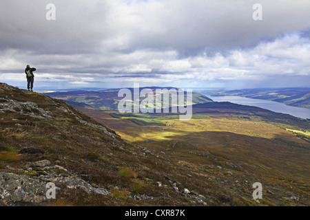A woman taking a photo Meallfuarvonie or Meall Fuar-mhonaidh with views of Loch Ness and the Great Glen near to Drumnadrochit Inverness-shire Scotland Stock Photo