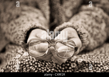 Hands of an old woman holding old broken glasses, sepia processing Stock Photo