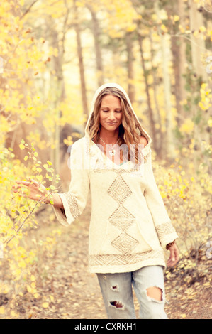 Natural casual woman in a jeans and sweater walking through the yellow autumn leaves. Stock Photo