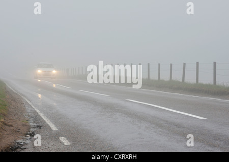 Car travelling with headlights on in dense fog on a road in the Scottish Highlands, Grampian Mountains, Scotland, United Kingdom Stock Photo