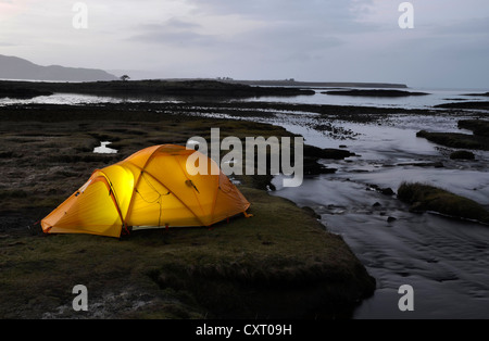 Yellow illuminated expedition tent, trekking tent, on a river estuary, at dusk, Isle of Skye, Scotlan, United Kingdom, Europe Stock Photo