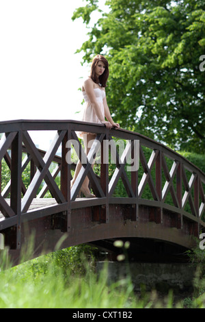 Young woman wearing a short beige summer dress and high heels standing on a wooden bridge Stock Photo