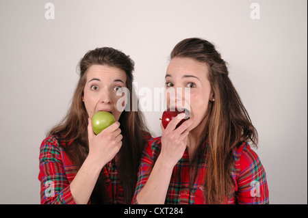 Twin sisters, one with a red apple, the other with a green apple Stock Photo