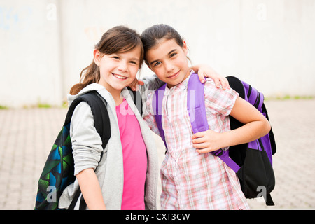 Two girls standing arm in arm on their way to school Stock Photo