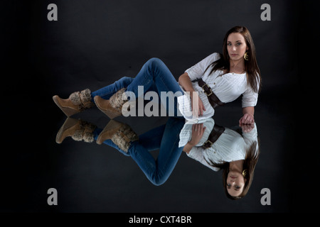 Young woman wearing a white top and jeans, lying on a mirror, mirrored image Stock Photo