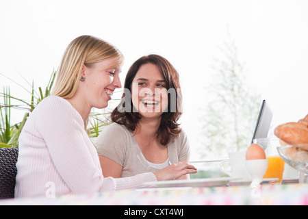 Two young women using a laptop while having breakfast on a terrace Stock Photo