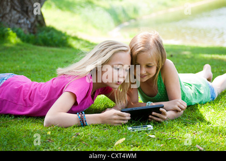 Girls lying on a meadow and chatting with a tablet PC Stock Photo