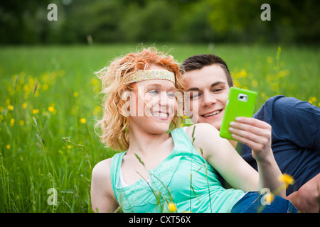 Young couple lying on a meadow and checking an SMS on a mobile phone Stock Photo