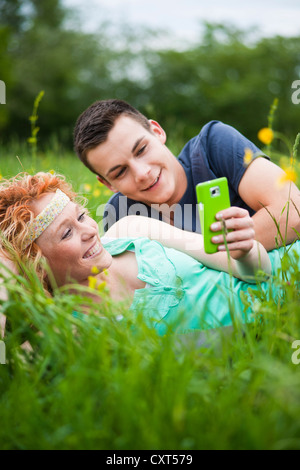 Young couple lying on a meadow and checking an SMS on a mobile phone Stock Photo