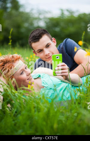 Young couple lying on a meadow and checking an SMS on a mobile phone Stock Photo
