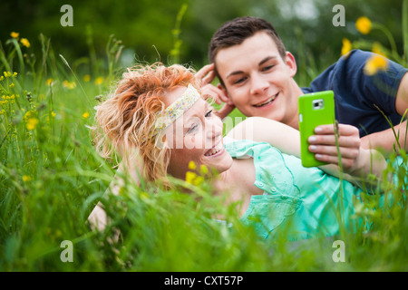 Young couple lying on a meadow and checking an SMS on a mobile phone Stock Photo