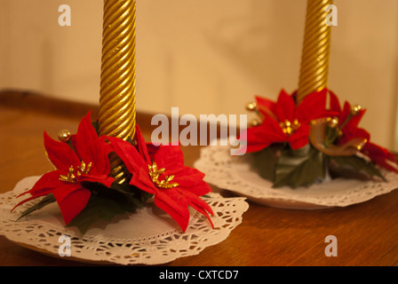 The bases of two gold twisted Christmas candles with red poinsettia  flower decorations on doilies on wood surface Stock Photo