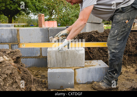 Bricklayer using Lump Hammer to level Concrete block when building foundation wall Stock Photo