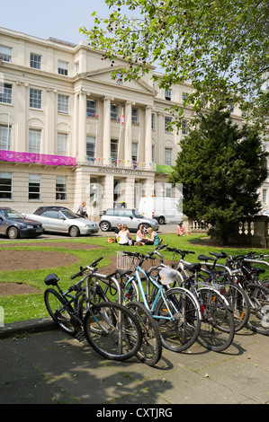 dh The Promenade CHELTENHAM GLOUCESTERSHIRE Girls sitting relaxing on grass and bicycles bike stand Municipal Offices Stock Photo
