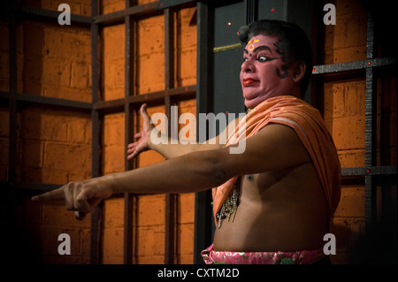 Horizontal close up portrait of a Kathakali performance artist partially made up as Minukku practising facial gestures on stage. Stock Photo