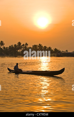 Vertical view of a glorious sunset in the backwaters of Kerala with a fisherman paddling his canoe in the foreground. Stock Photo