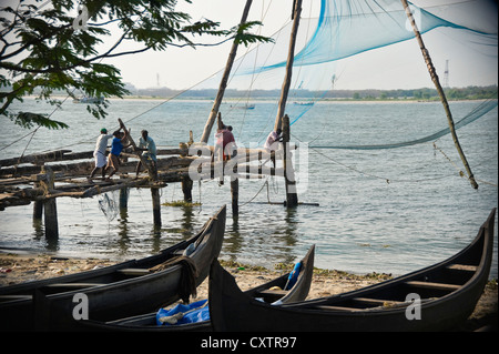 Horizontal wide angle landscape of fishermen lowering a Chinese fishing net into the water at Fort Cochin. Stock Photo