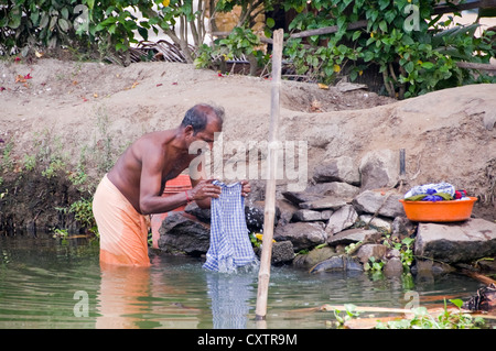 Horizontal portrait of an Indian man washing his clothes on the riverbank in Kerala. Stock Photo