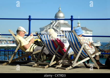 Horizontal portrait of several elderly people sitting on deckchairs enjoying the view of the pier and seaside on a sunny day Stock Photo