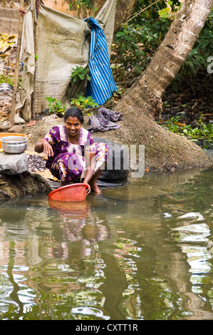 Vertical portrait of a young Indian woman cleaning mussels at the riverbank in Kerala. Stock Photo