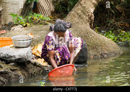 Horizontal portrait of a young Indian woman cleaning mussels by the river side in Kerala. Stock Photo