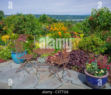Vashon-Maury Island, WA: Iron table and chairs on flagstone patio with a view of a terraced garden and of Quartermaster Harbor Stock Photo